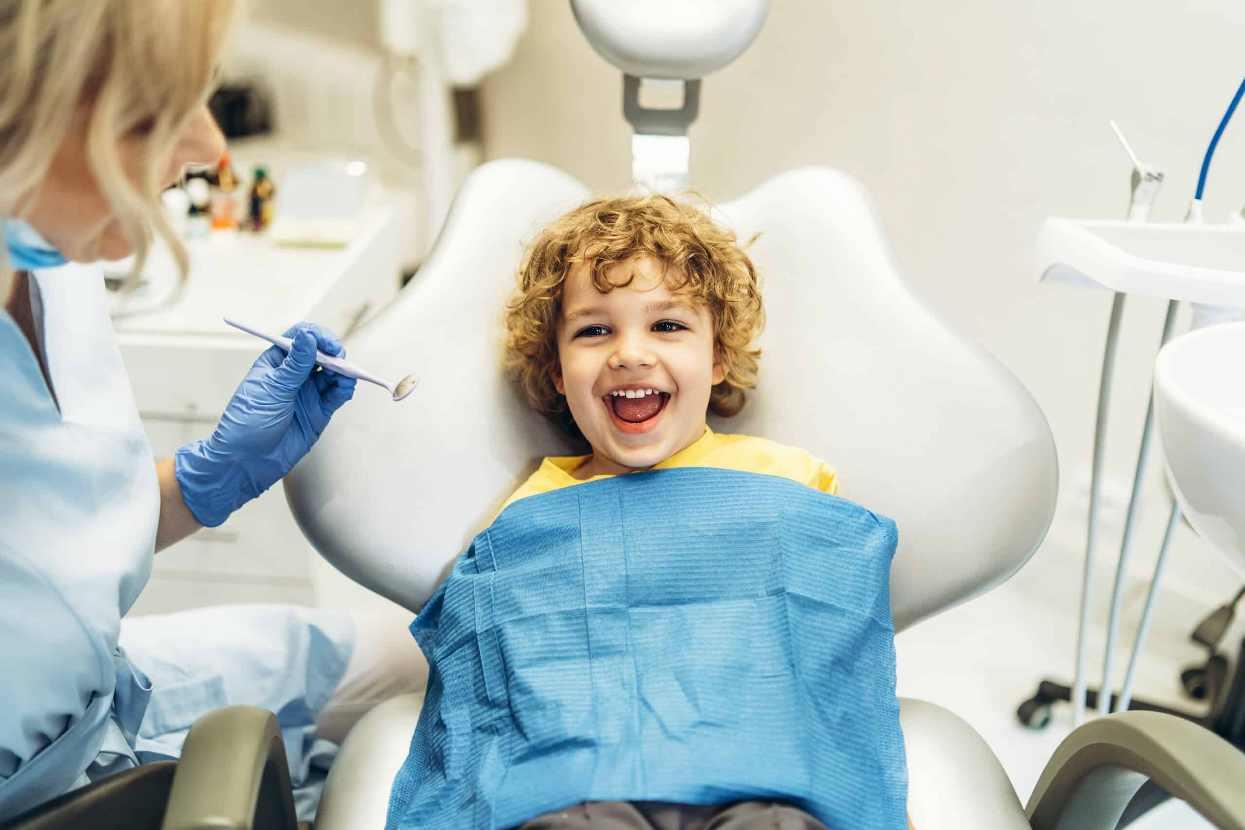 Cute young boy visiting dentist, having his teeth checked by fem